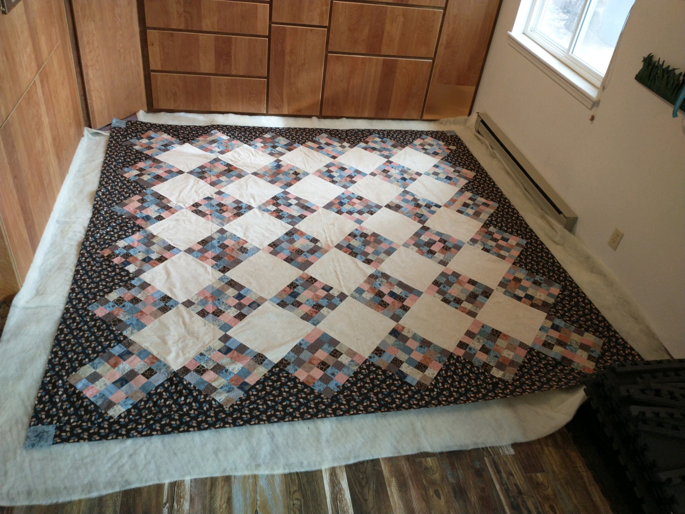 quilt top, batting, and backing laid out on the floor for basting